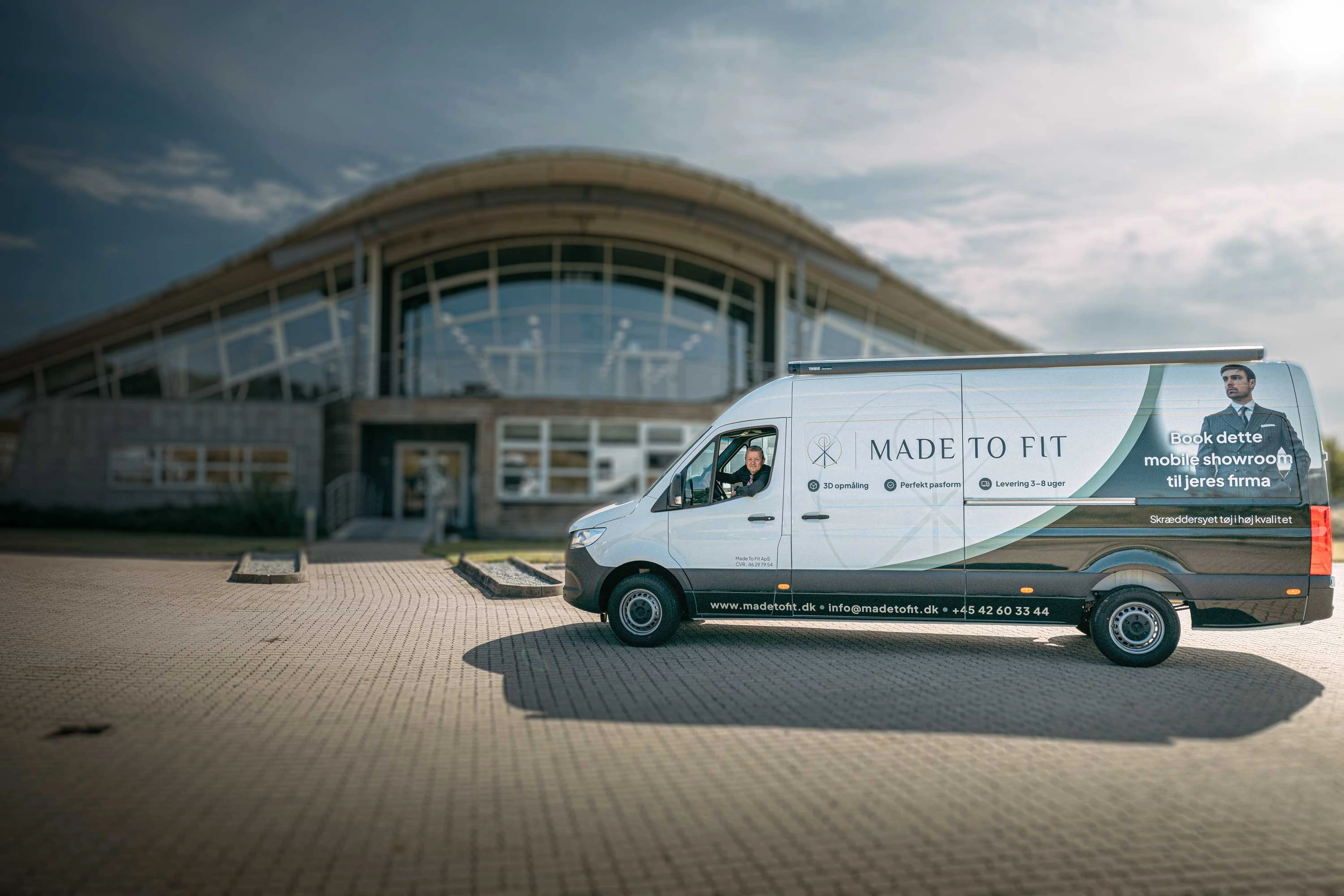 Het mobiele showroom van Made To Fit – de bestelbus voor een kantoorpand met een medewerker achter het stuur.